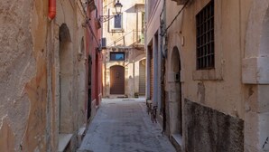 A narrow alleyway with buildings on either side, a cobblestone path, and a closed shop at the end.