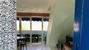 A room with a tiled floor, a dining area with chairs and a table, a television on a stand, and a blue door.