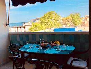 A balcony table set with plates, cups, and a fruit basket, overlooking a pool and buildings. - Viareggio Città Giardino sea view apartment with terrace (Viareggio)