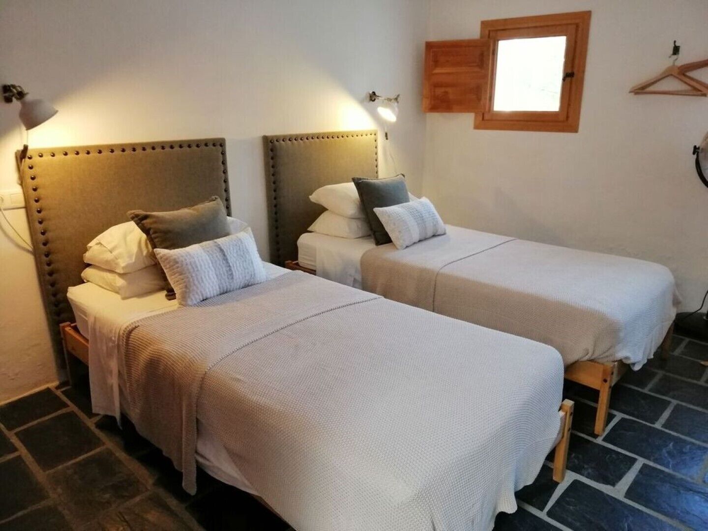 A room with two beds, each with a headboard and pillows, a small window, and a wall-mounted light fixture.