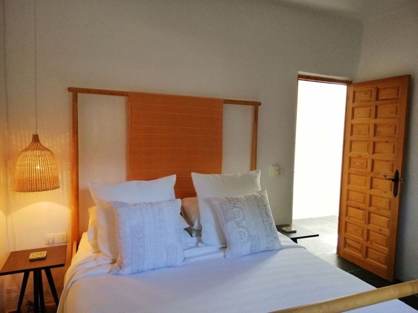 Ein Schlafzimmer mit einem hölzernen Kopfteil, einem Bett mit weißer Bettwäsche, einem Nachttisch mit Lampe und einer Holztür.