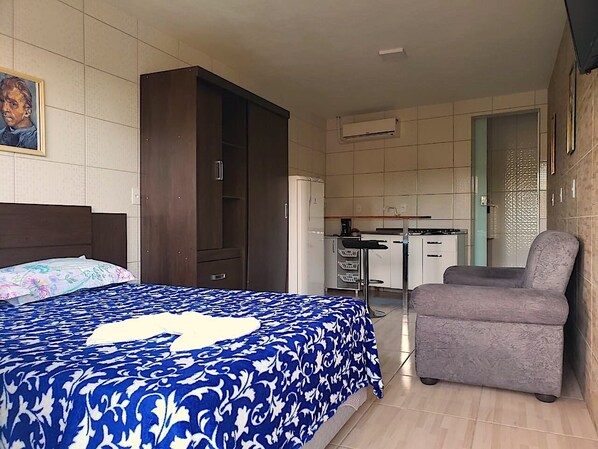 A bedroom with a bed, a chair, a wardrobe, and a kitchenette. - Casa Verde (Blumenau)