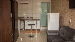 Un espacio habitable compacto con kitchenette, un sofá y una puerta de vidrio que da al baño.