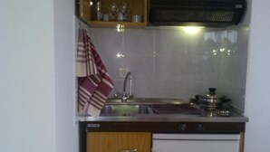A compact kitchen with wooden cabinets, a built-in stove, and a dishwasher. - Evdokia Studios (Sifnos)