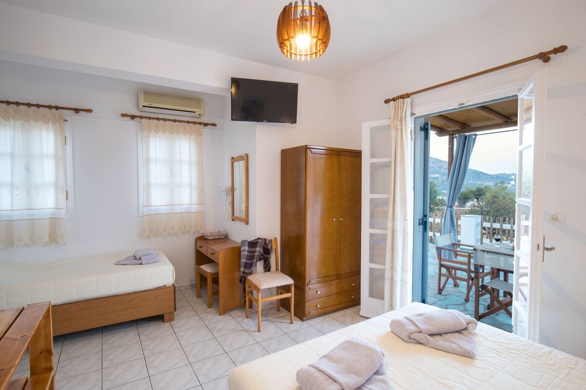 A bedroom with a bed, a desk, a chair, a wardrobe, and a balcony with a table and chairs.