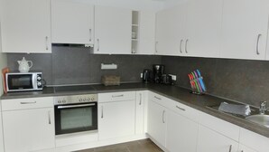 Una cocina moderna con armarios blancos, horno integrado, microondas y cafetera.