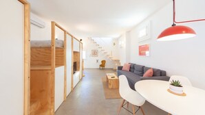 A modern interior with a bunk bed, a sofa, a dining table, and a staircase.