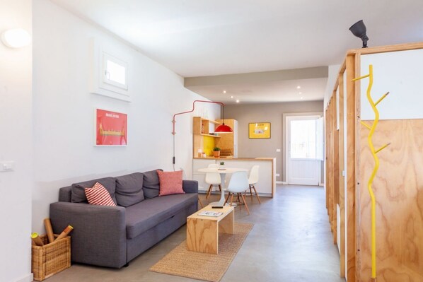 A modern living room with a grey sofa, a wooden coffee table, and a dining area with a white table and chairs.