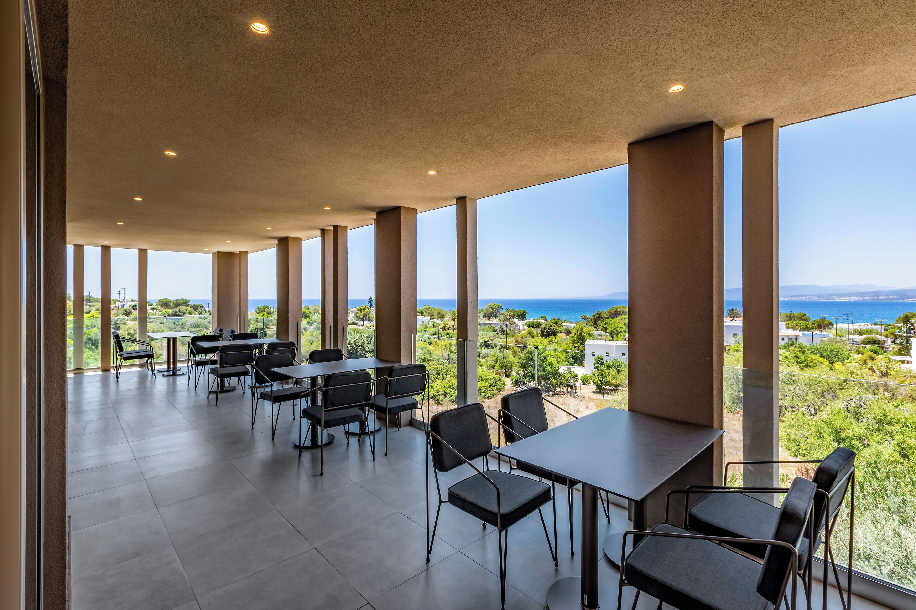 A spacious outdoor dining area with large windows, a view of the sea, and a modern architectural design.
