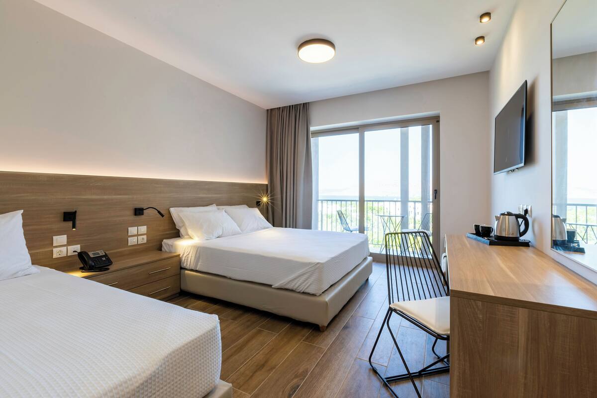 A hotel room with two beds, a desk, a chair, a TV, and a balcony with a view.