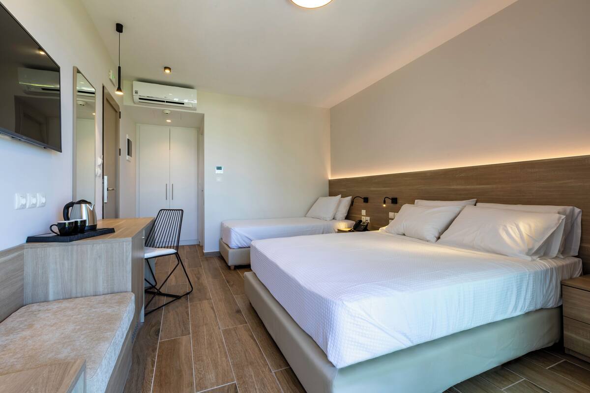 A modern hotel room with a large bed, bedside tables, a desk with a chair, and an air conditioning unit.