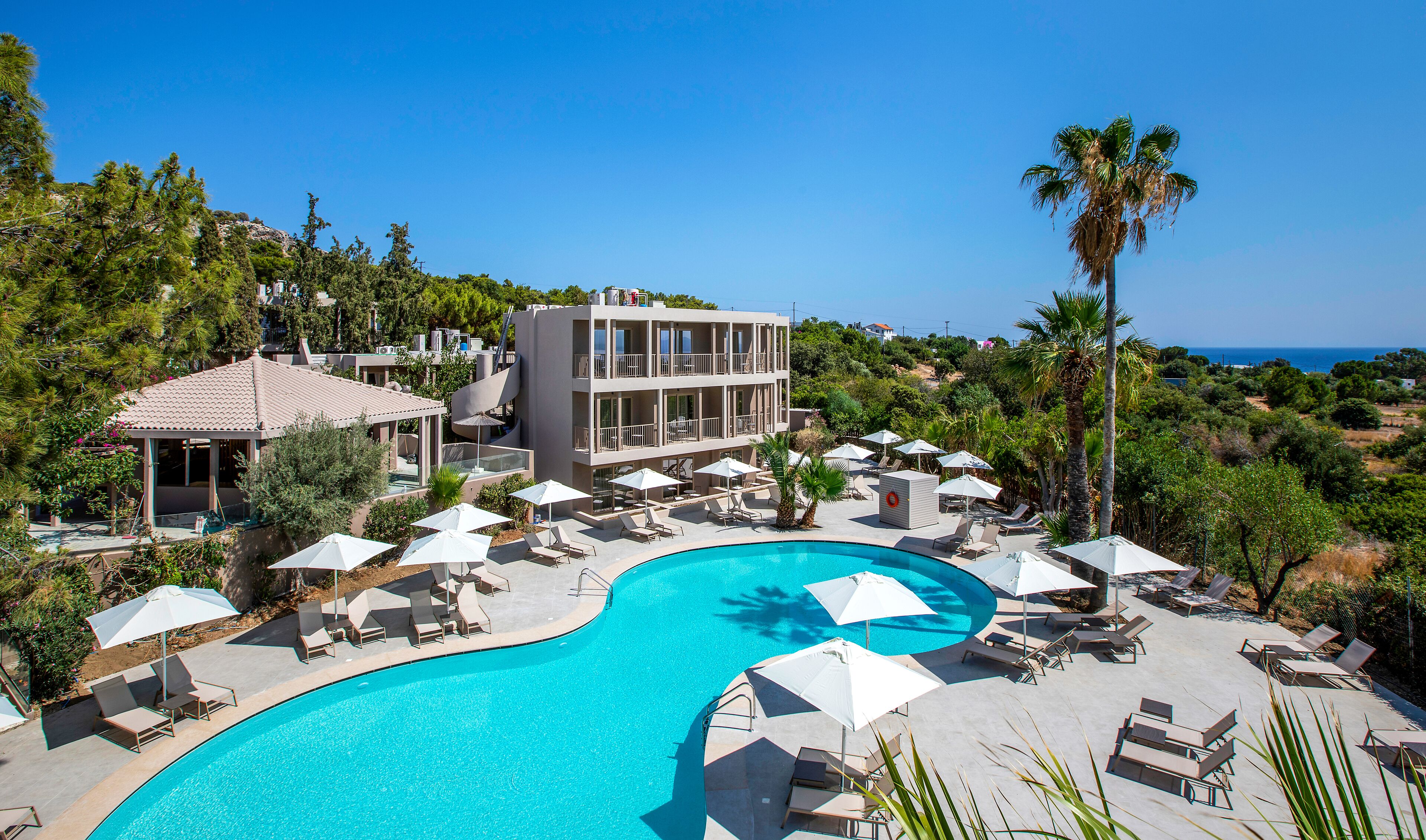 A resort with a large pool, sun loungers, umbrellas, and a view of the ocean.