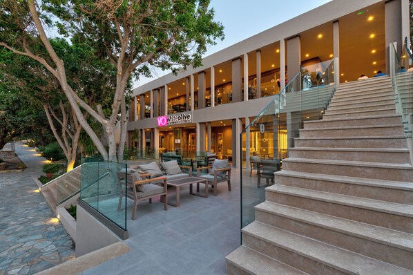 A modern building with a glass exterior, outdoor seating area, and a staircase leading to an upper level. - White Olive Premium Lindos - All Inclusive (Rhodes)