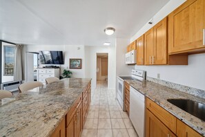 A modern kitchen with granite countertops, wooden cabinets, and a built-in microwave. - Block to Beach! Koko Resorts at the Waikiki Banyan 30th Floor Deluxe Ocean View,Free parking & Wifi (Honolulu)