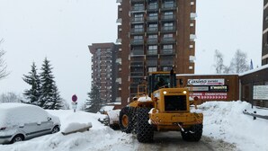 Una máquina quitanieves despeja una carretera con un edificio de varios pisos al fondo.