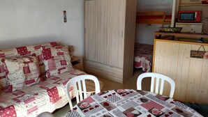 Una habitación acogedora con un armario de madera, una cama con colcha, una mesa de comedor con mantel a cuadros y una kitchenette con microondas.