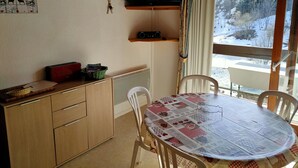 Una habitación acogedora con techo de madera, un televisor montado en la pared, una mesa con mantel a cuadros y una ventana con vistas a un paisaje nevado.