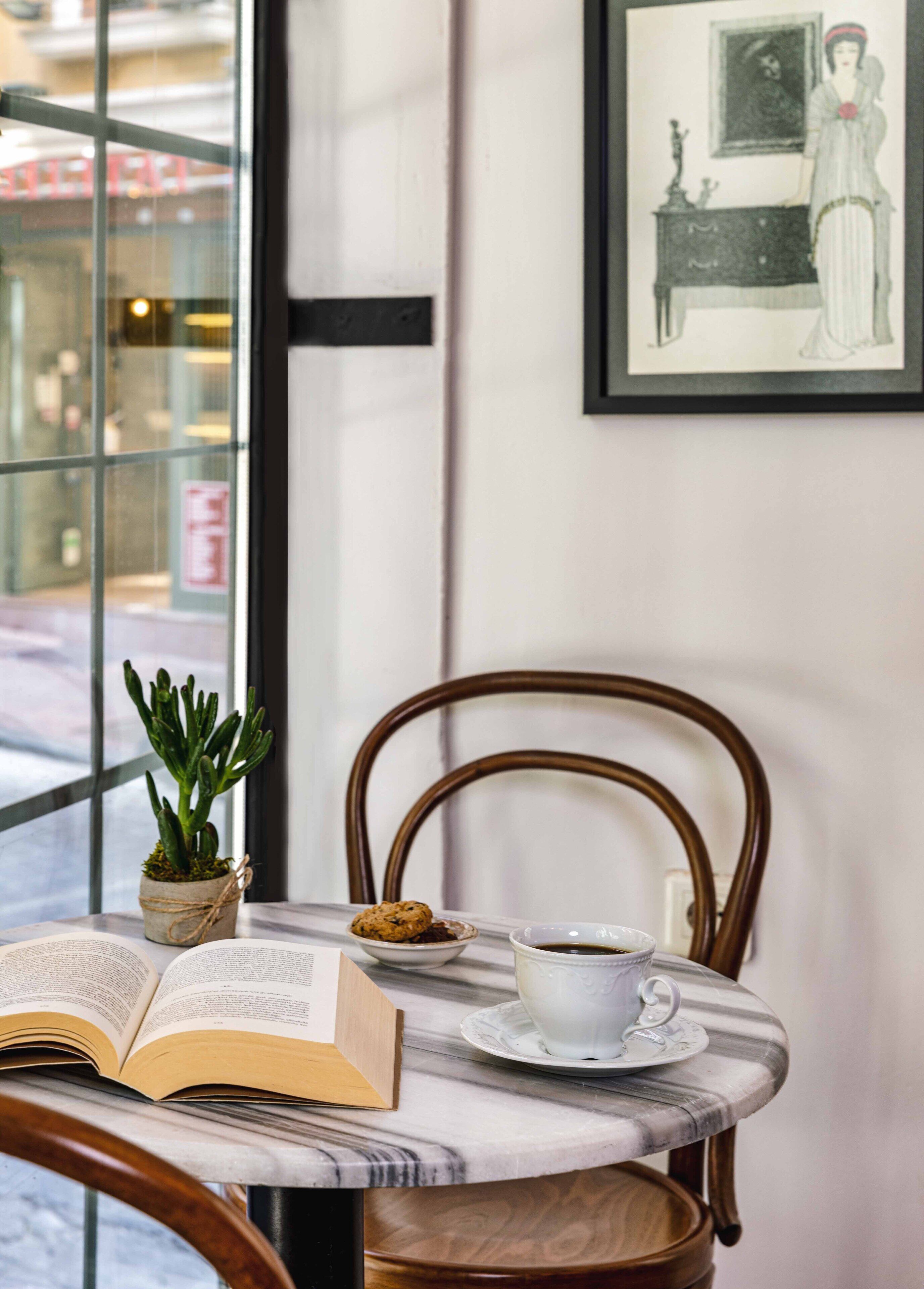 Une table avec un livre, une tasse de café et une petite plante.