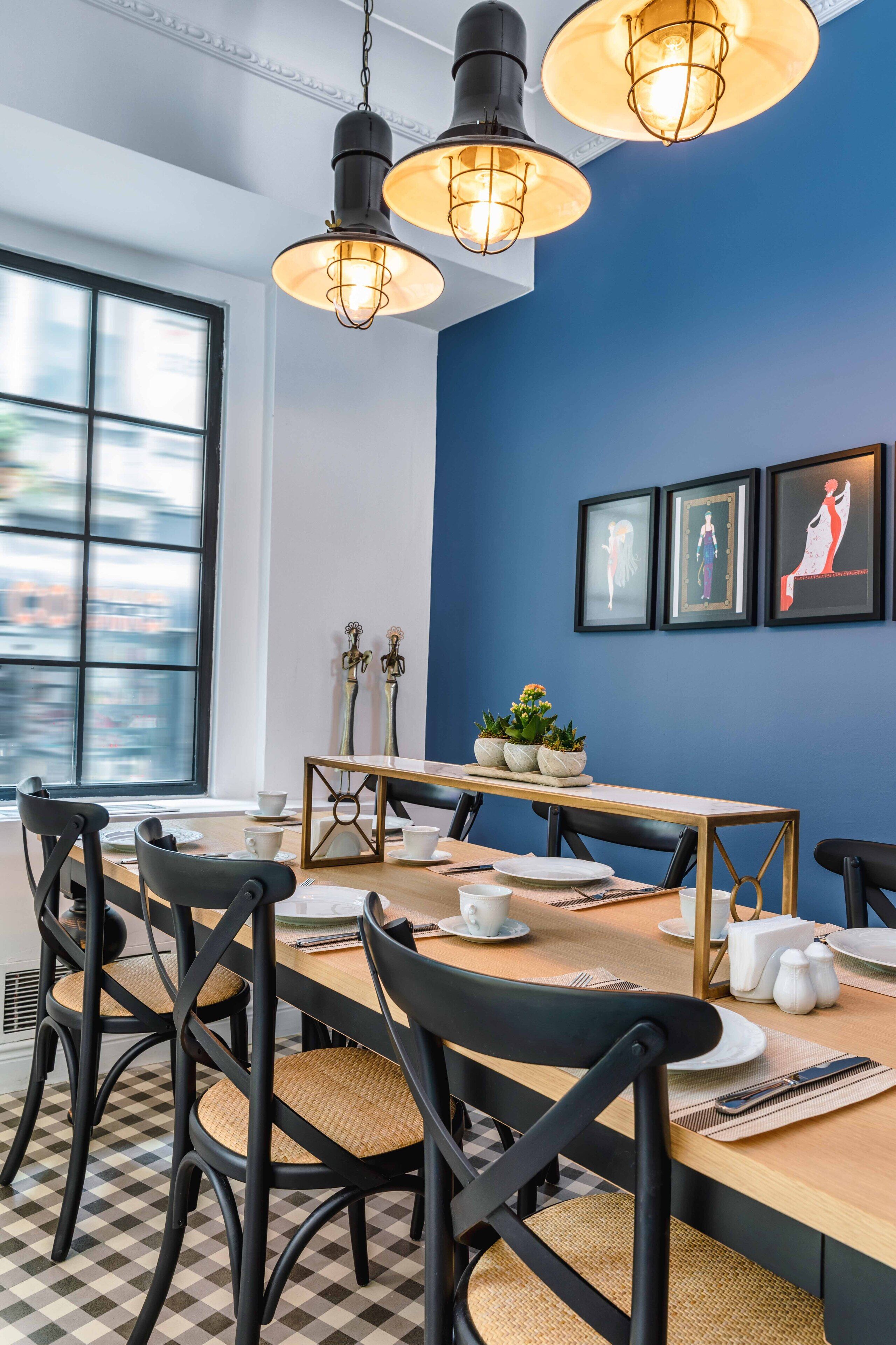 A dining area with a checkered floor, black chairs, a wooden table set for four, and pendant lighting.