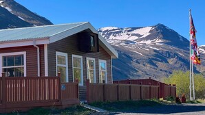 A wooden building with a sloped roof, a flagpole with multiple flags, and a mountainous backdrop. - Engimýri Lodge (Bakki)