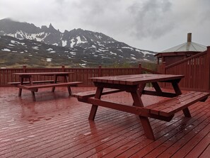 A wooden deck with picnic tables and a gazebo, overlooking a mountainous landscape with snow patches. - Engimýri Lodge (Bakki)
