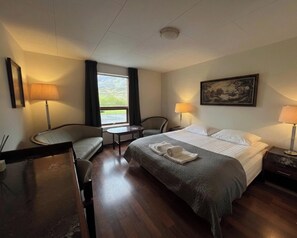 A hotel room with a bed, two chairs, a small table, a window with curtains, a painting on the wall, and a lamp on each side of the bed. - Engimýri Lodge (Bakki)