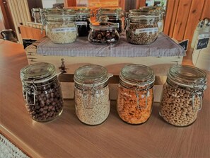 A display of various food items in glass jars with labels, arranged on a wooden counter.
