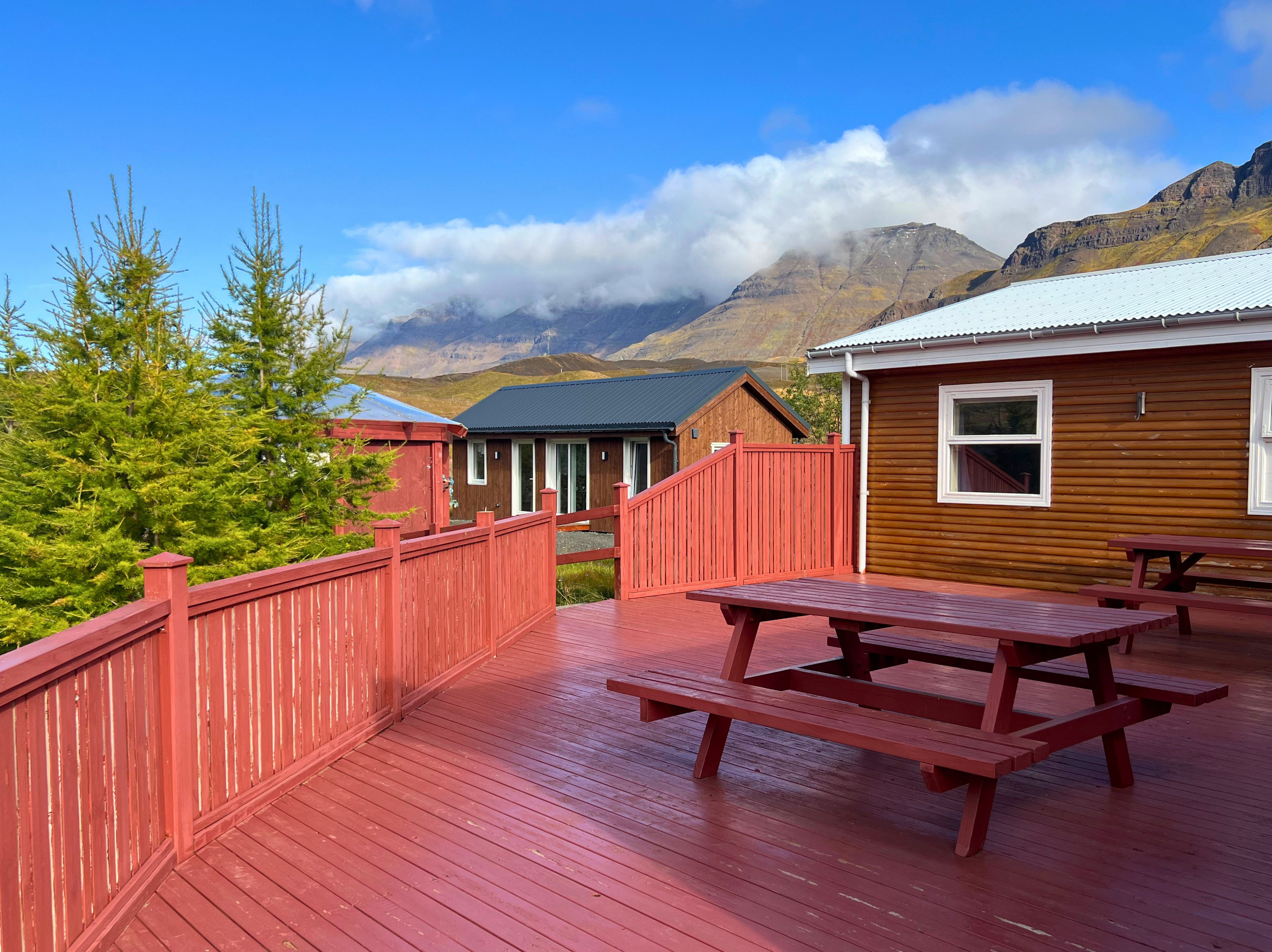 Une terrasse en bois avec des tables de pique-nique, des chalets aux boiseries blanches et une vue imprenable sur les montagnes.