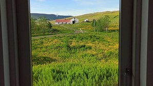 A view through a window of a rural landscape with a barn and rolling hills. - Engimýri Lodge (Bakki)