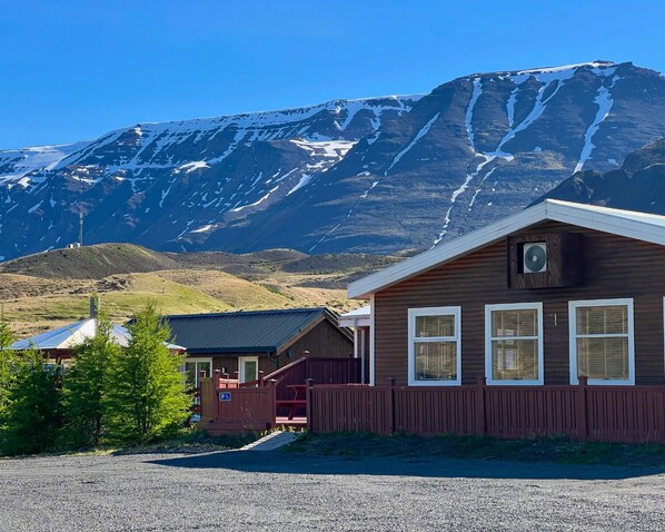 A wooden cabin with a gravel driveway, a fenced area, and a mountain backdrop. - Engimýri Lodge (Bakki)