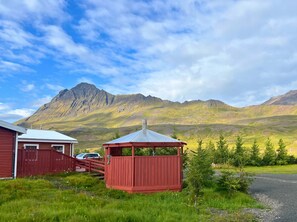 A red wooden structure with a metal roof, a red building with a white roof, and a mountain range in the background.