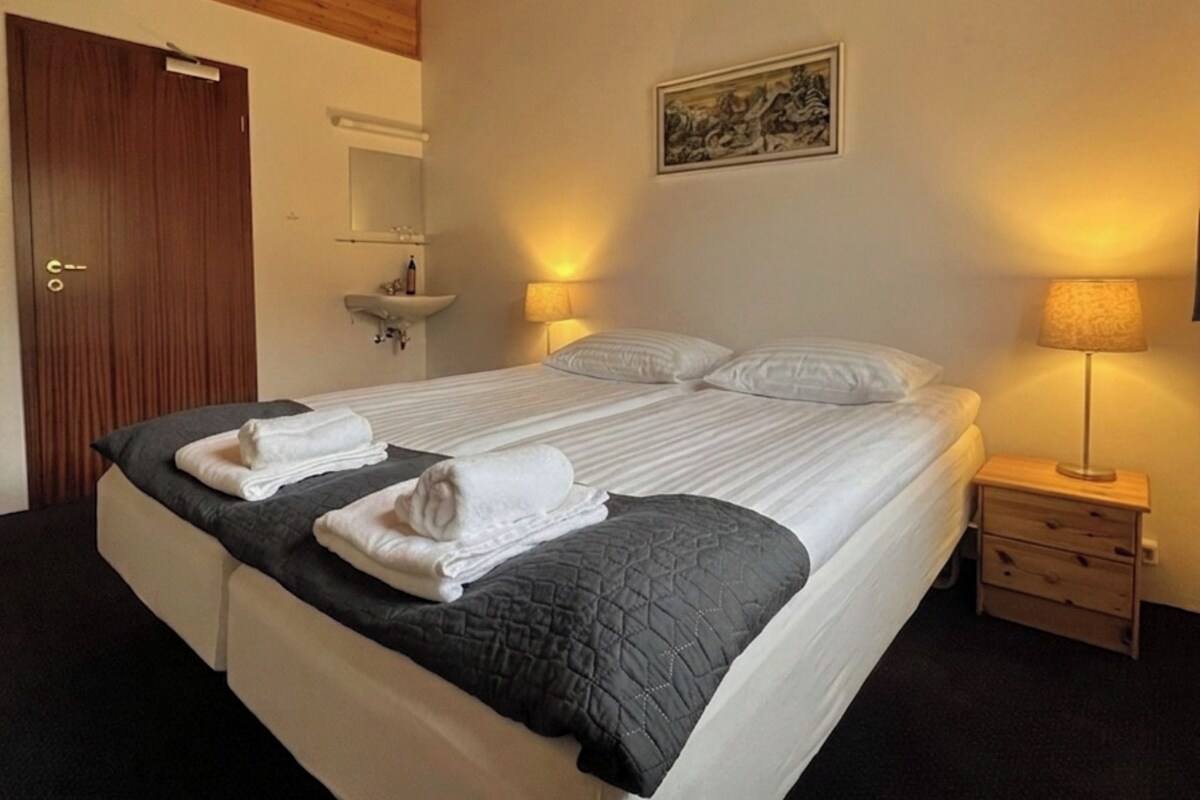 Een hotelkamer met een houten plafond, een bed met witte lakens, een nachtkastje met een lamp en een schilderij aan de muur.