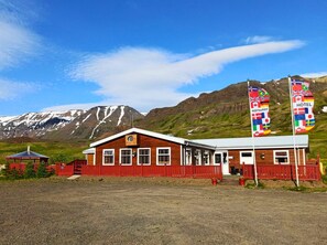 A wooden building with a red fence, flags, and a mountain backdrop.
