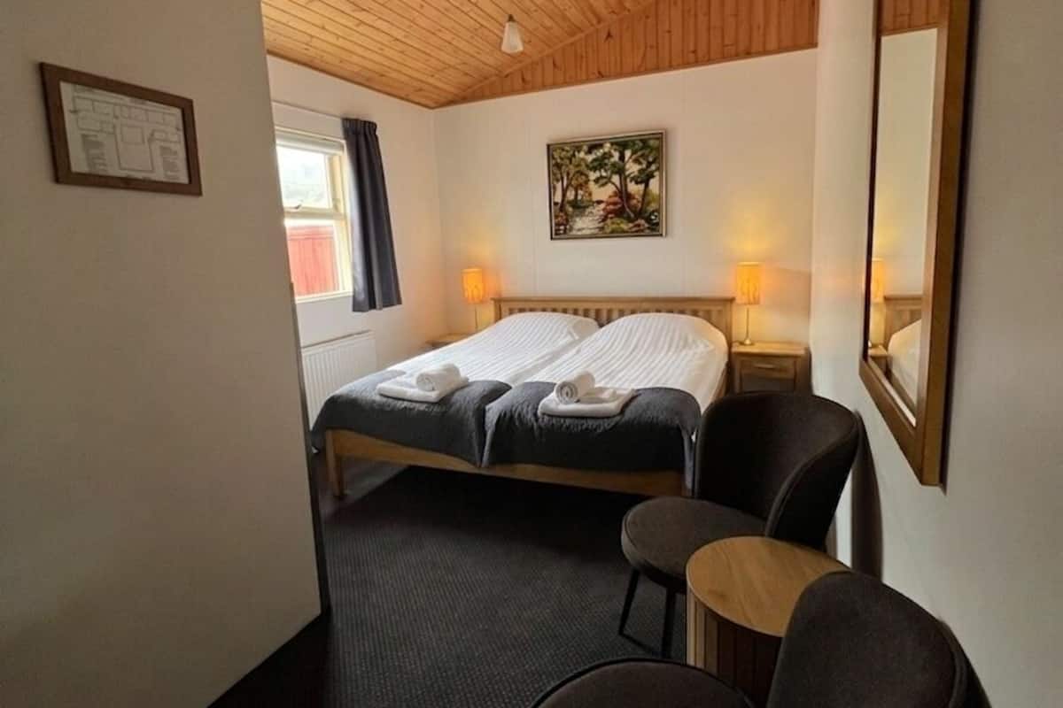 Una habitación de hotel con techo de madera, una cama con sábanas blancas, una mesita y una silla.