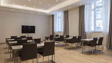 Un salón de conferencias con mesas y sillas, un televisor de pantalla plana y ventanas grandes con cortinas.