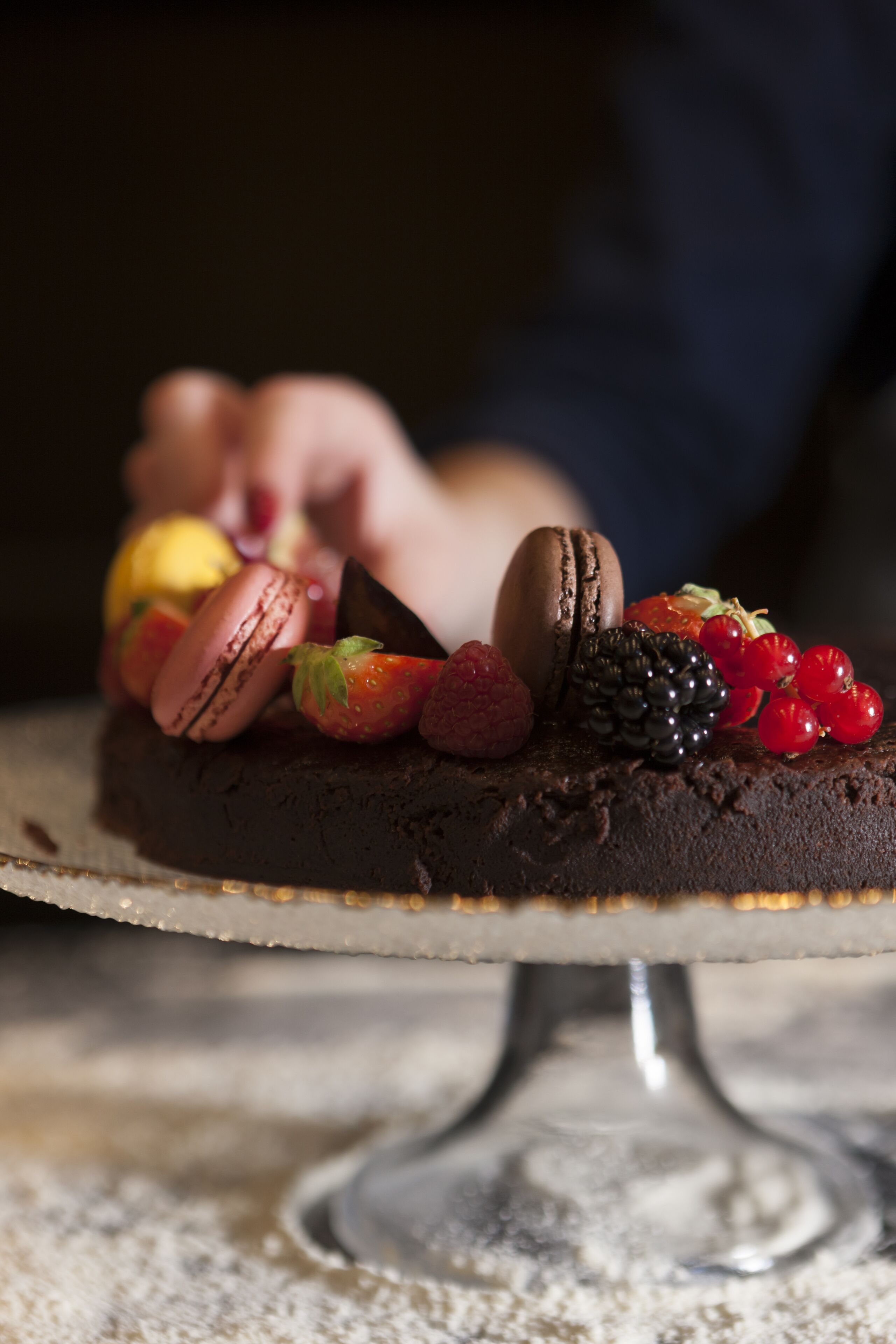 Un pastel de chocolate con fresas, frambuesas, zarzamoras y macarons sobre un soporte para pasteles.