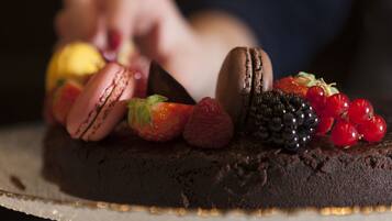 Un pastel de chocolate con fresas, frambuesas, zarzamoras y macarons sobre un soporte para pasteles.