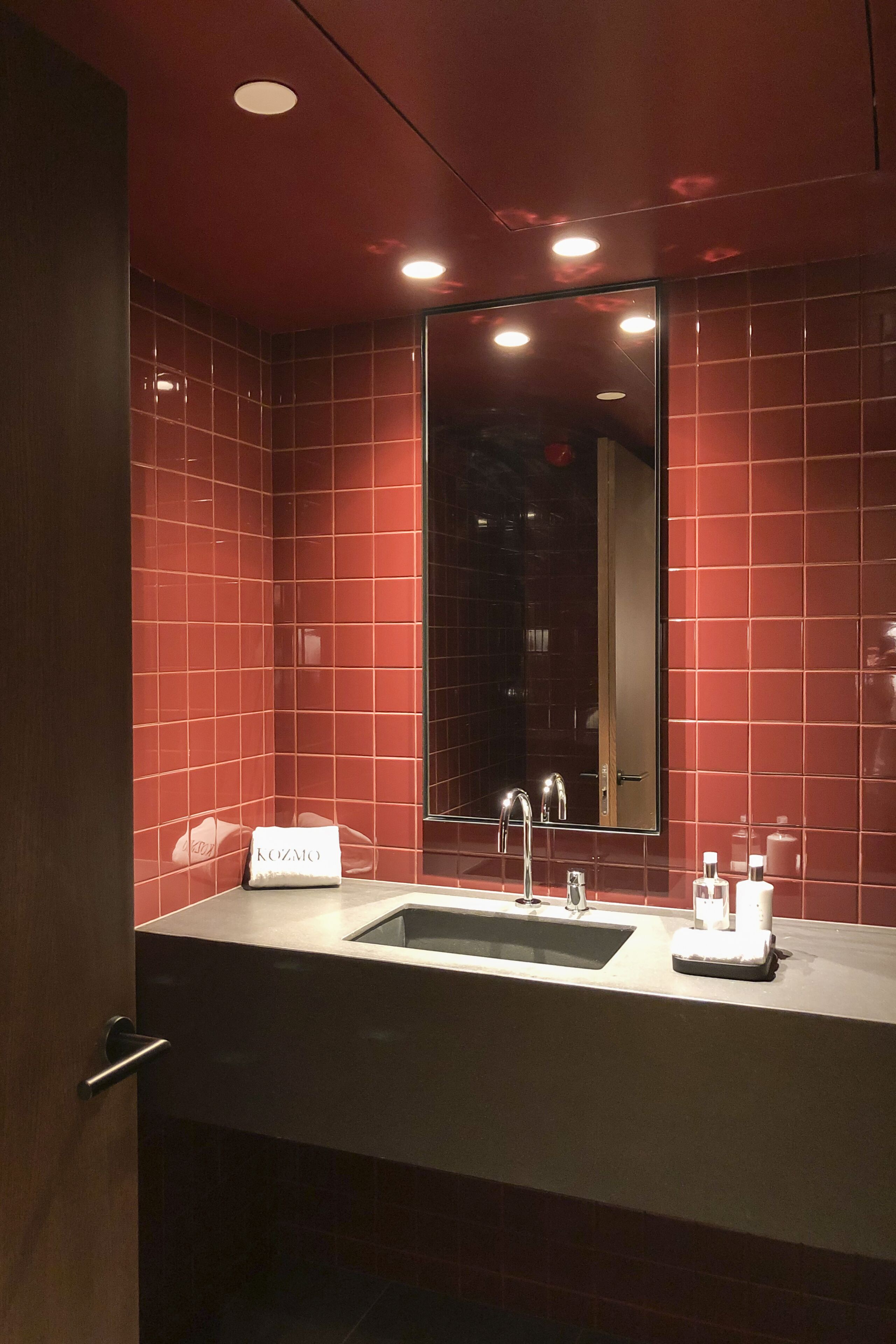 Une salle de bain moderne avec des carreaux rouges, un grand miroir, un lavabo avec une serviette et des articles de toilette.