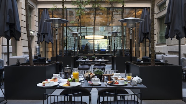 Een terras met tafels, stoelen, parasols en uitzicht op een gebouw door glazen wanden.