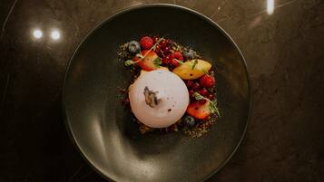 Un postre en un plato oscuro con varias frutas y bayas.
