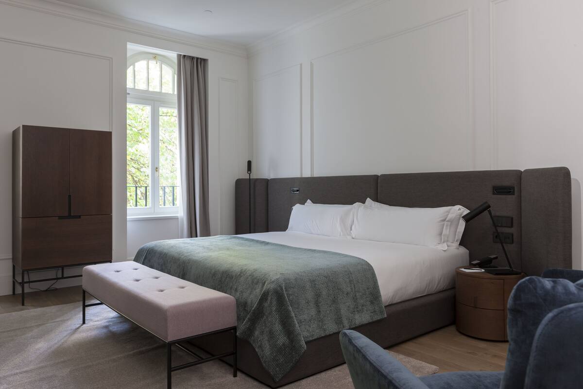 A modern bedroom with a large bed, a bedside table, a bench, and a wardrobe.