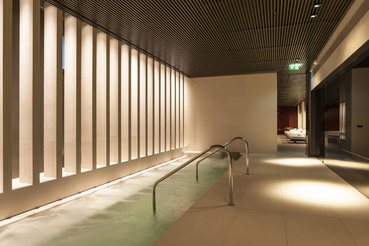 A corridor with a modern design, featuring a series of vertical light panels on the left and a metal handrail on the right.
