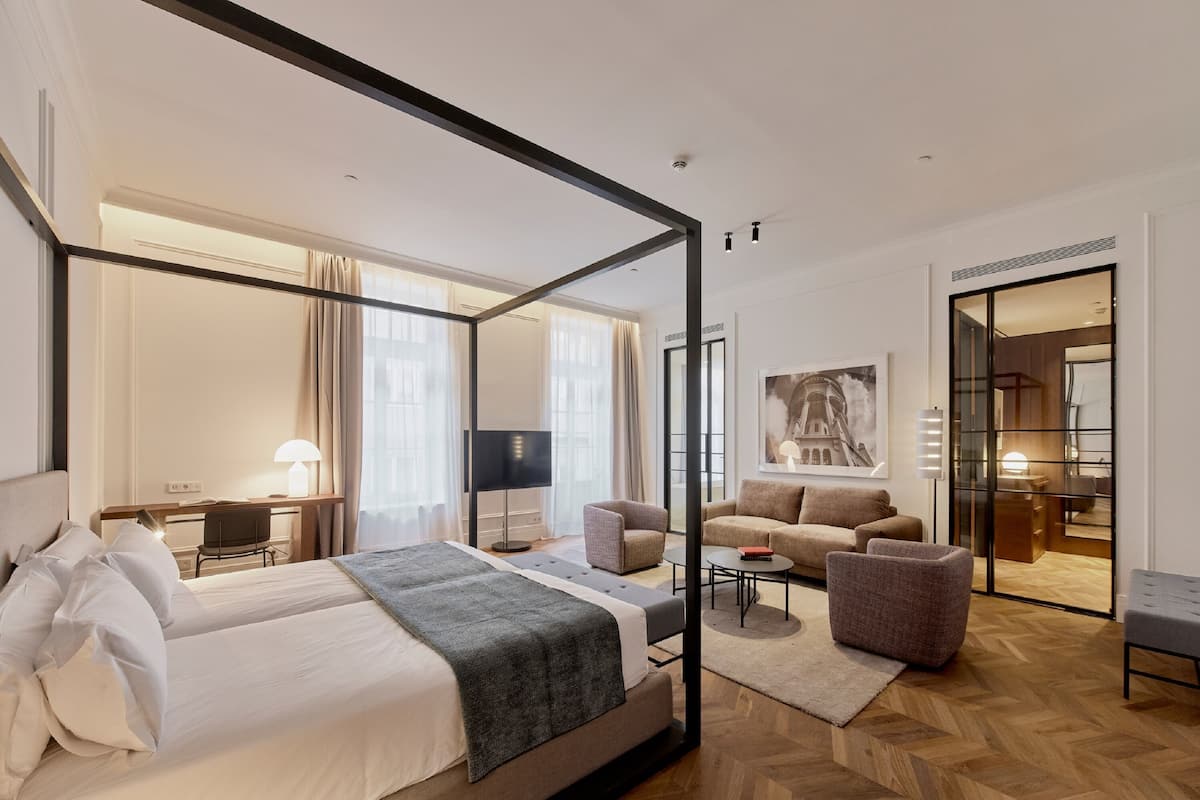 A modern hotel room with a four-poster bed, a sofa, a desk, and a large mirror.