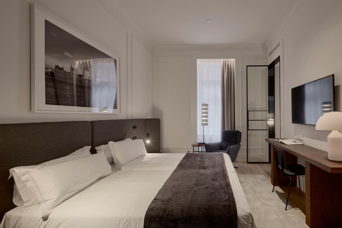 A hotel room with a large bed, a desk with a chair, a TV, and a window with curtains.