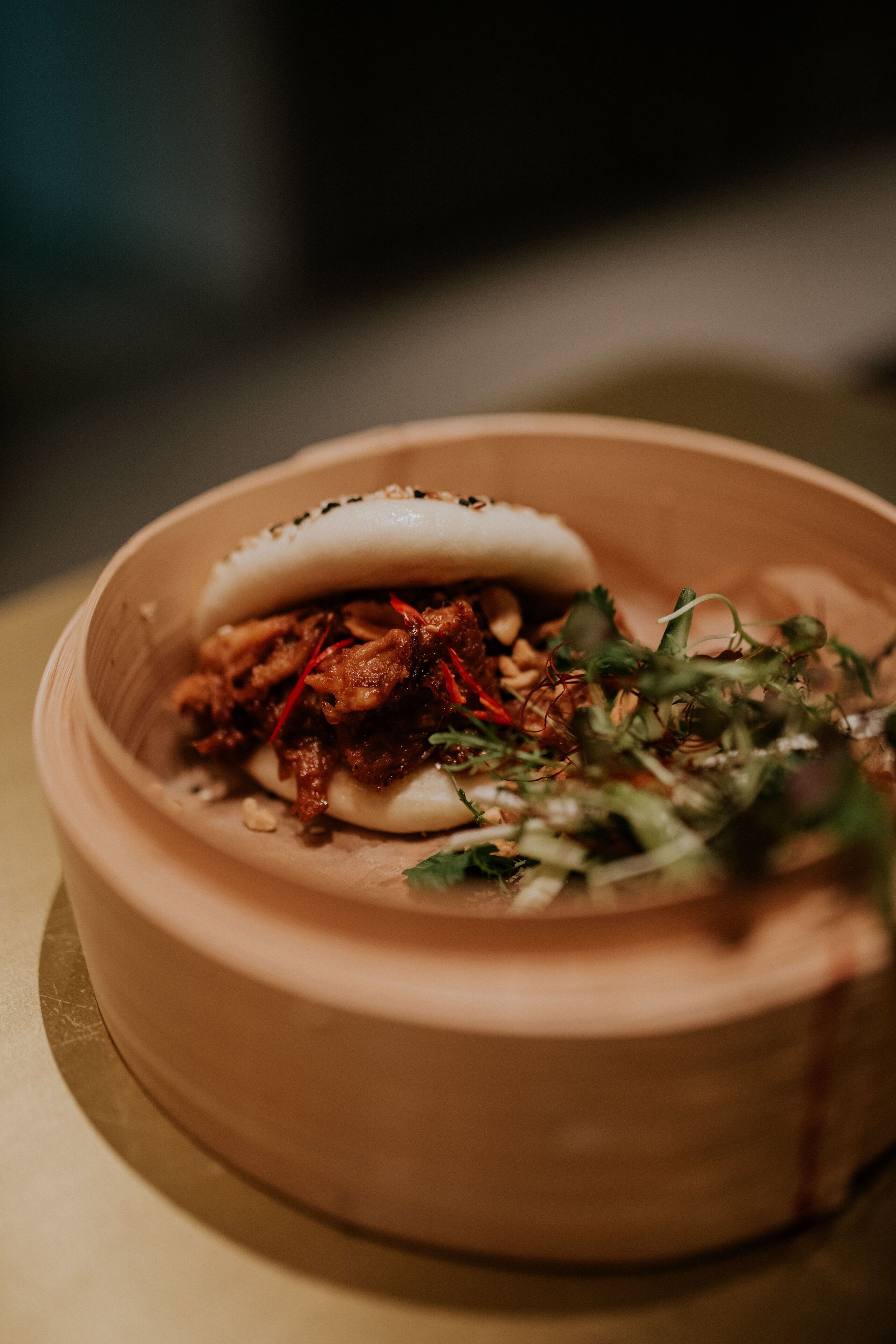 A bowl of food with a bun, meat, and greens.