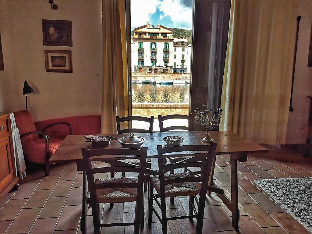 A dining area with a table and chairs, a red chair, a lamp, and a view of buildings through a window.