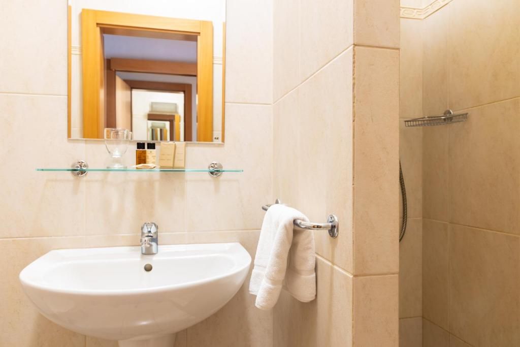 A bathroom with a white sink, a glass shelf above it, and a towel rack.