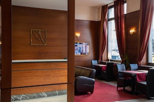 Um hall de hotel com balcão de recepção, área de estar e grandes janelas com cortinas.