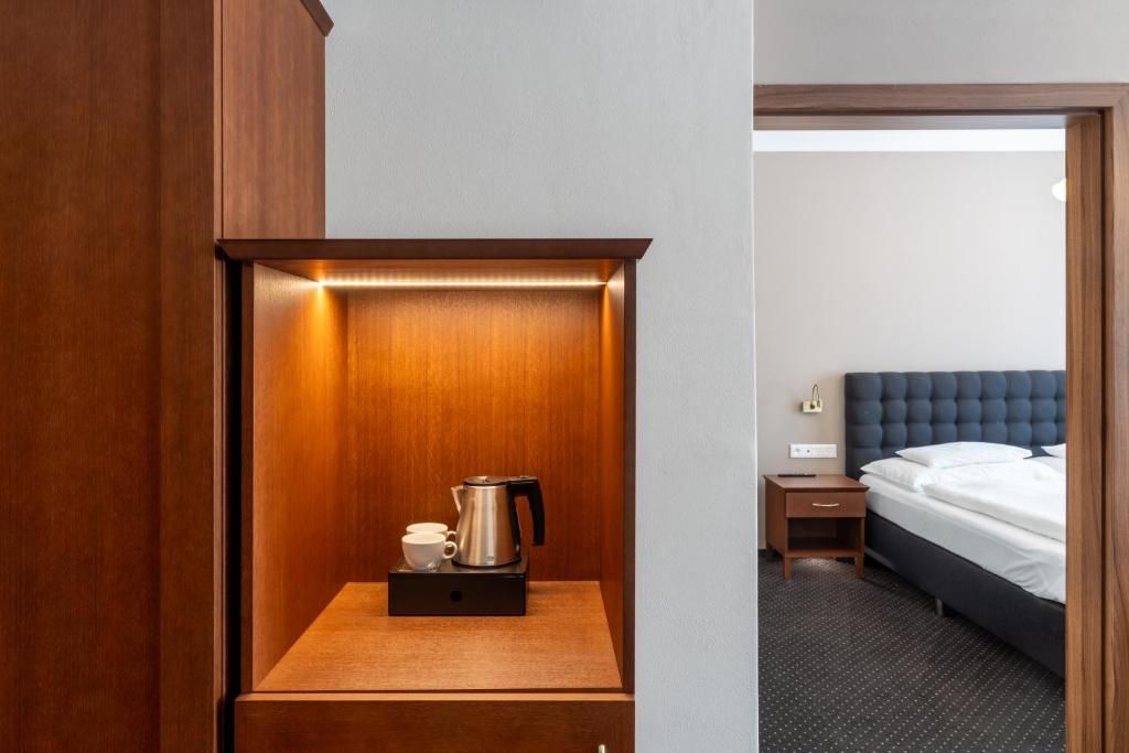 Habitación de hotel con un armario de madera, una mesita de noche con hervidor, una taza y un cajón pequeño.