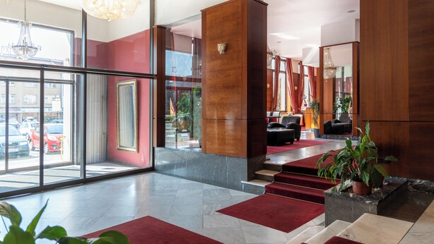Een moderne lobby met een rood tapijt, marmeren vloer en een kroonluchter.